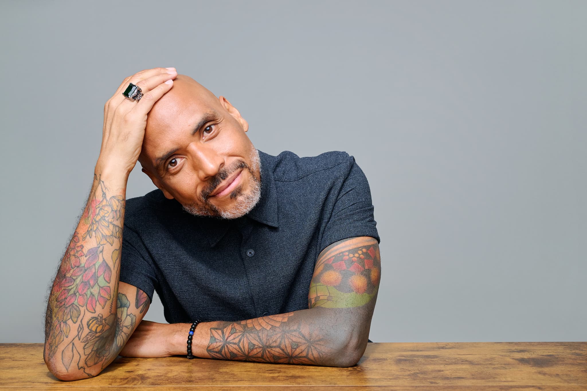 A man seated at a table rests his hand on his head.